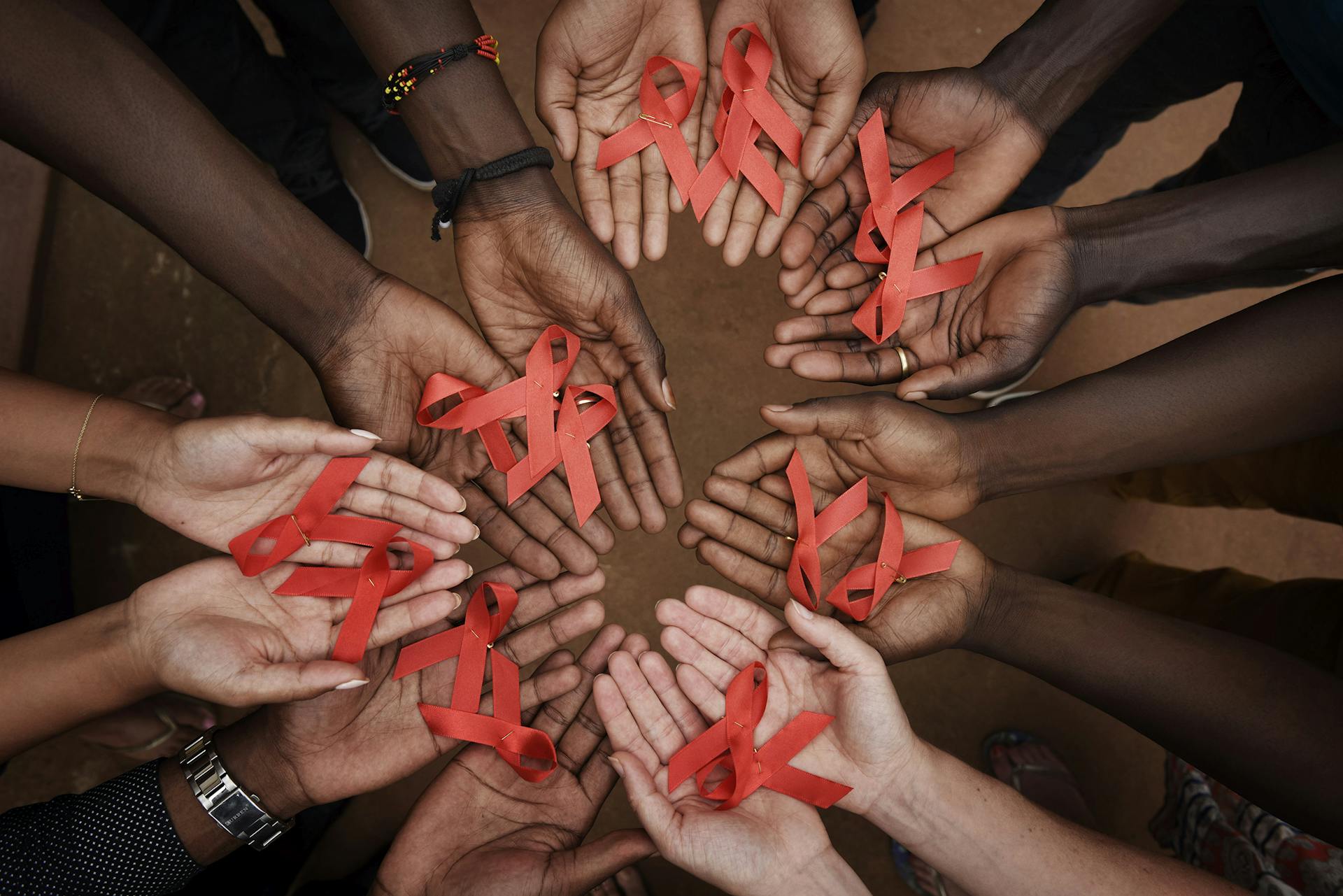 Handen met verschillende huidskleuren houden rode lintjes vast